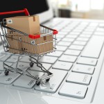 E-commerce. Shopping cart with cardboard boxes on laptop.