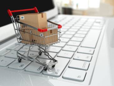 E-commerce. Shopping cart with cardboard boxes on laptop.